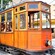 Pasajeros esperan en una parada ferroviaria dentro de un tranvía antiguo con ventanas abiertas